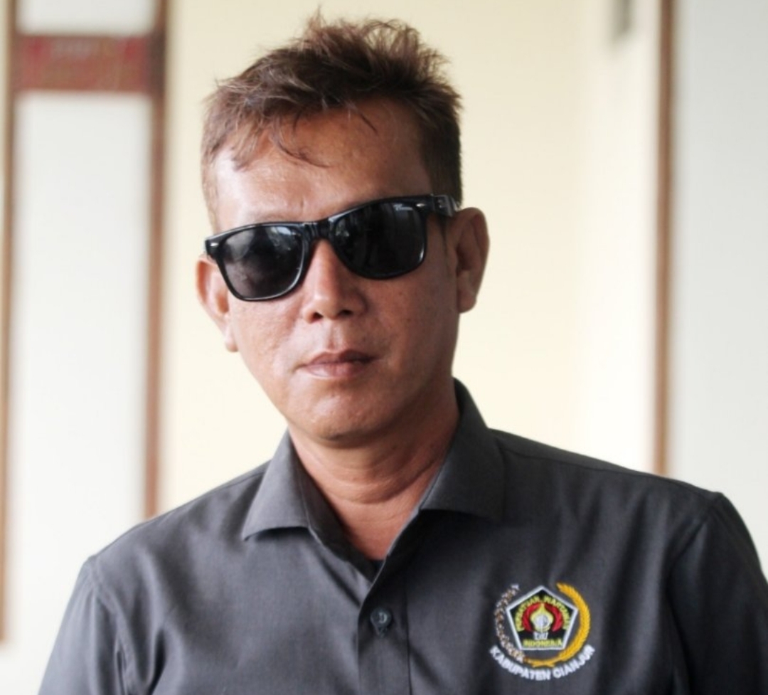 Nana Setiawan, Wakil Ketua PWI Kabupaten Cianjur, mengenakan kemeja PWI dan kacamata hitam saat memberikan pernyataan pers.