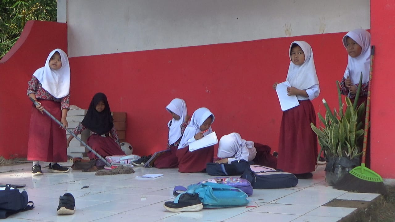 Siswa SDN Padangsari Cibeber belajar di lantai luar ruang sekolah karena ruang kelas rusak parah sejak 2022 tidak diperbaiki pemerintah.