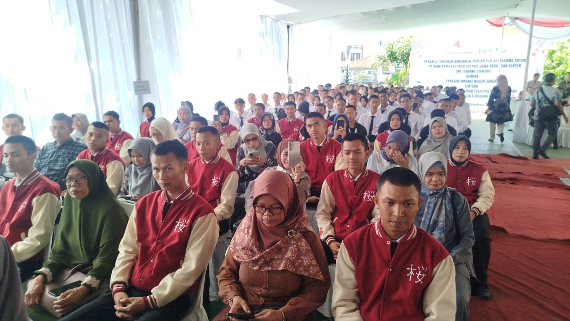 Teks: Peserta LPK Amanat Negeri Sakura di Cianjur mengenakan jaket merah saat mengikuti acara pelepasan pemberangkatan kerja ke Jepang bersama orang tua mereka.