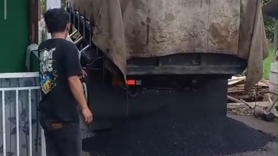 Teks: Proses pengaspalan jalan desa Sukataris menggunakan hotmix yang dikerjakan secara swakelola.