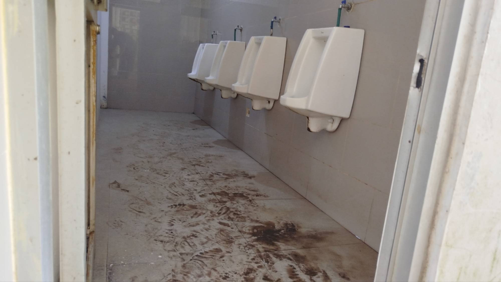 Teks: Toilet pria RSUD Pagelaran Cianjur kotor dengan lantai berlumpur dan noda kering terlihat jelas di area urinoir.