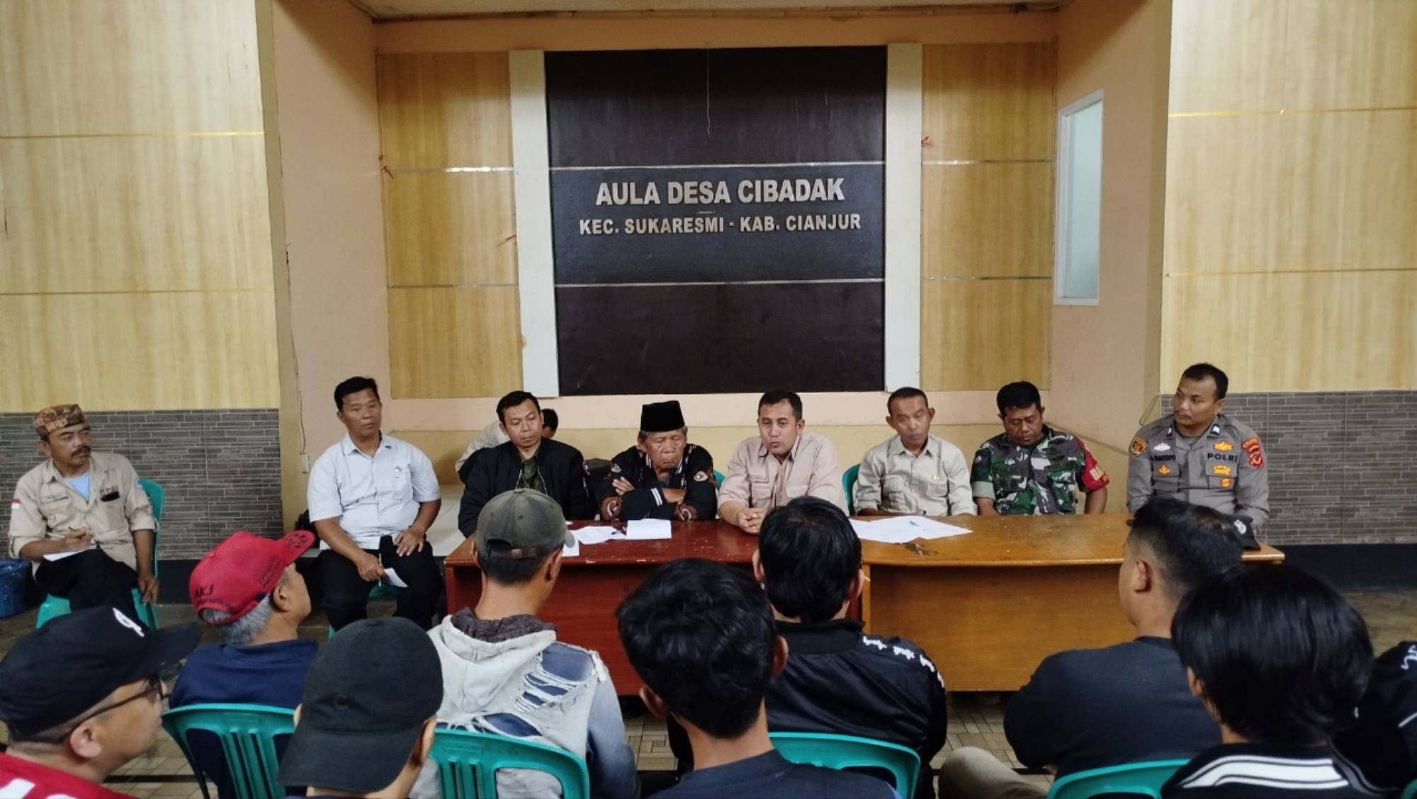 Teks: Suasana audiensi antara pemuda Desa Cibadak dan Pemerintah Desa di Aula Desa Cibadak terkait tuntutan transparansi anggaran.