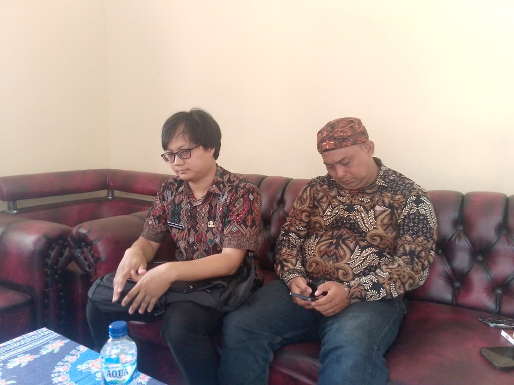 Teks: Dua pejabat desa duduk di ruang kantor saat menjelaskan status penerima PKH.