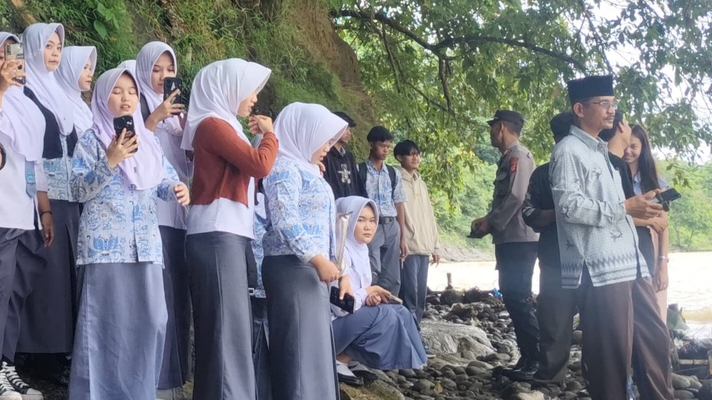 Teks: Pelajar dan warga berdiri di tepi Sungai Cibuni sebelum menyeberang menggunakan rakit.