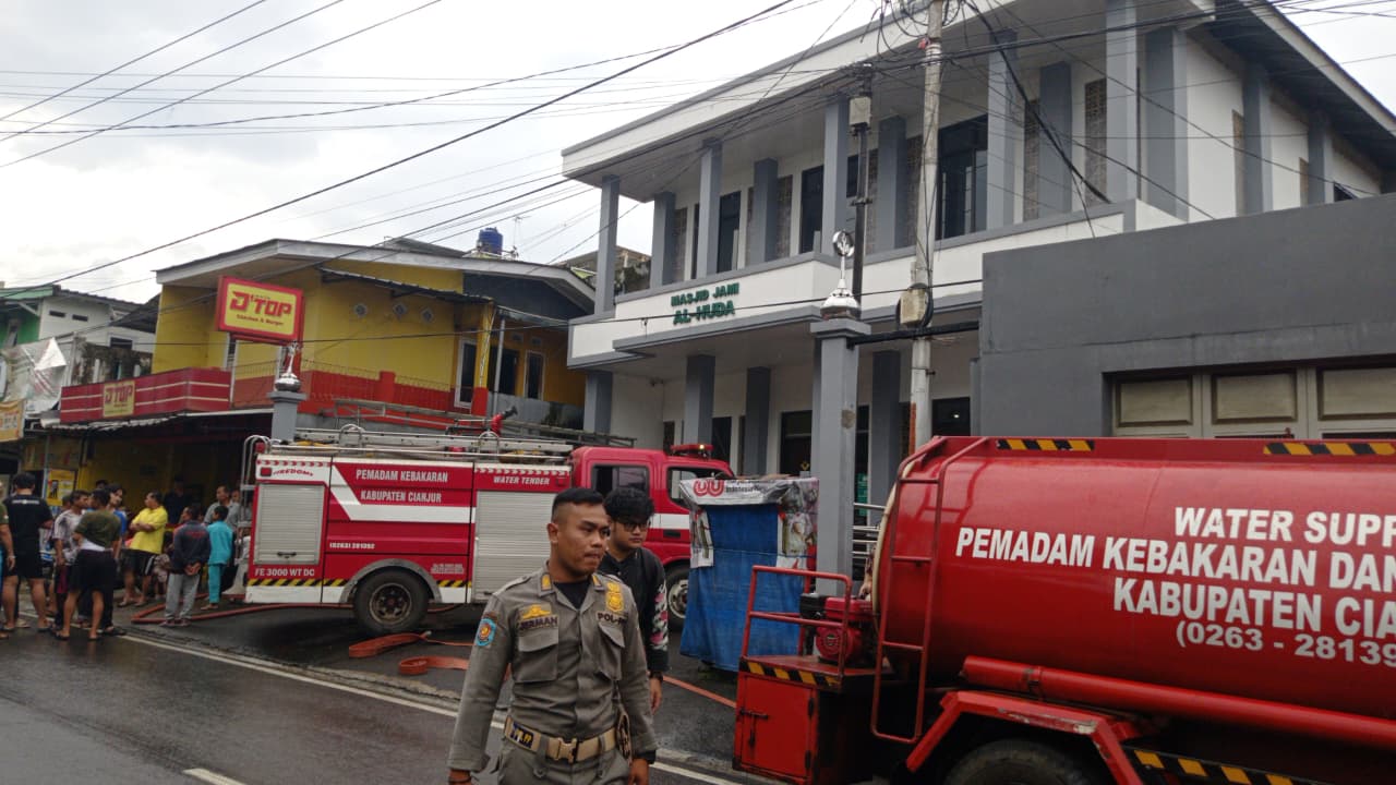 Teks: Mobil pemadam kebakaran Kabupaten Cianjur dan petugas berjaga di lokasi kebakaran Sawahgede.