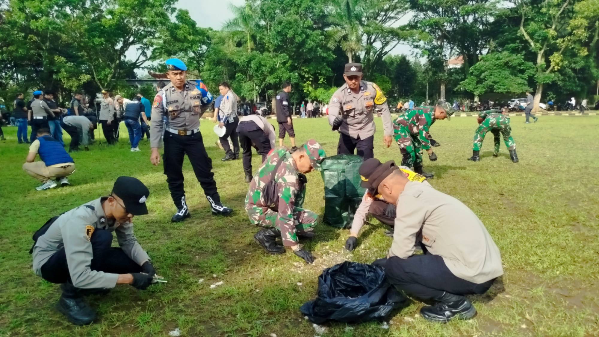 Teks: Personel Polri dan TNI membersihkan area rumput saat Aksi Bersih Cianjur di Taman Prawatasari.