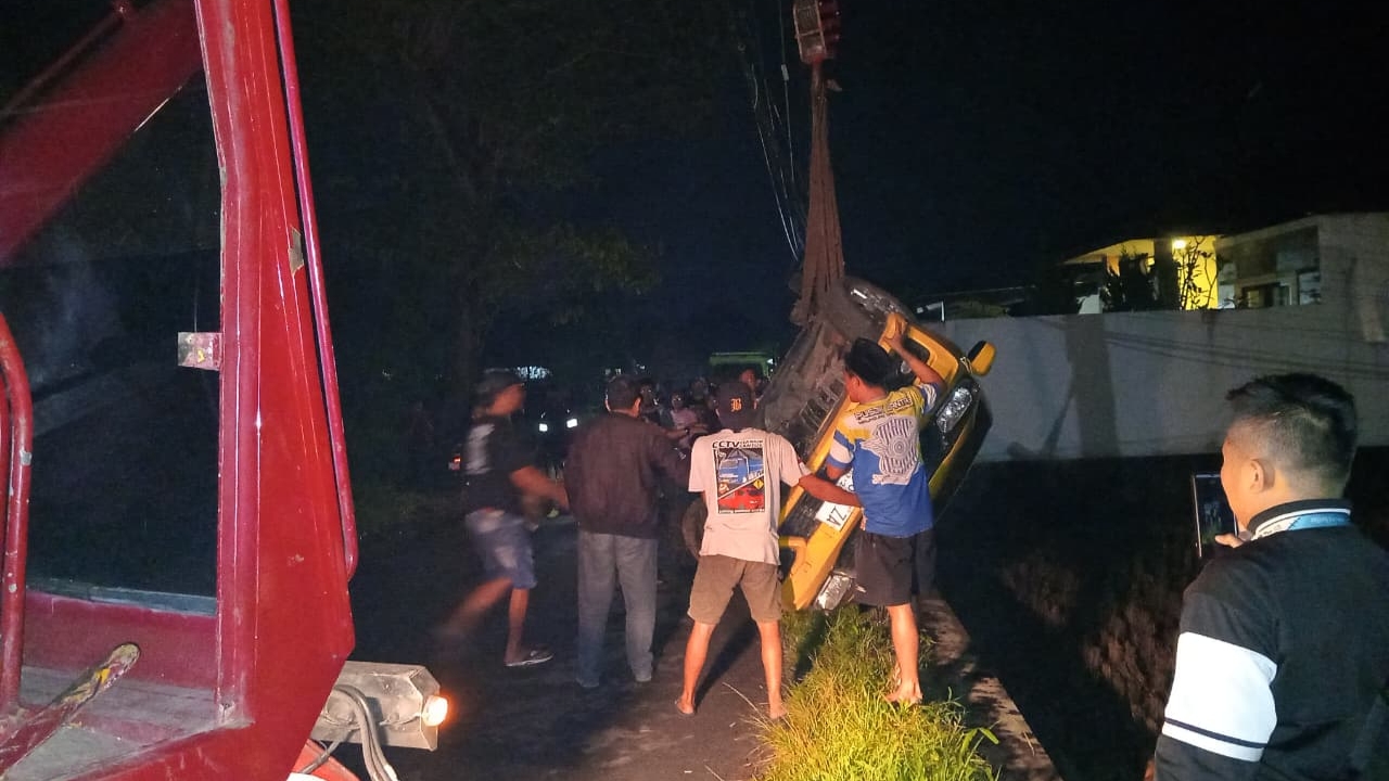 Teks: Evakuasi mobil Brio kecelakaan di Karangtengah Cianjur oleh petugas dan warga sekitar pada malam hari.