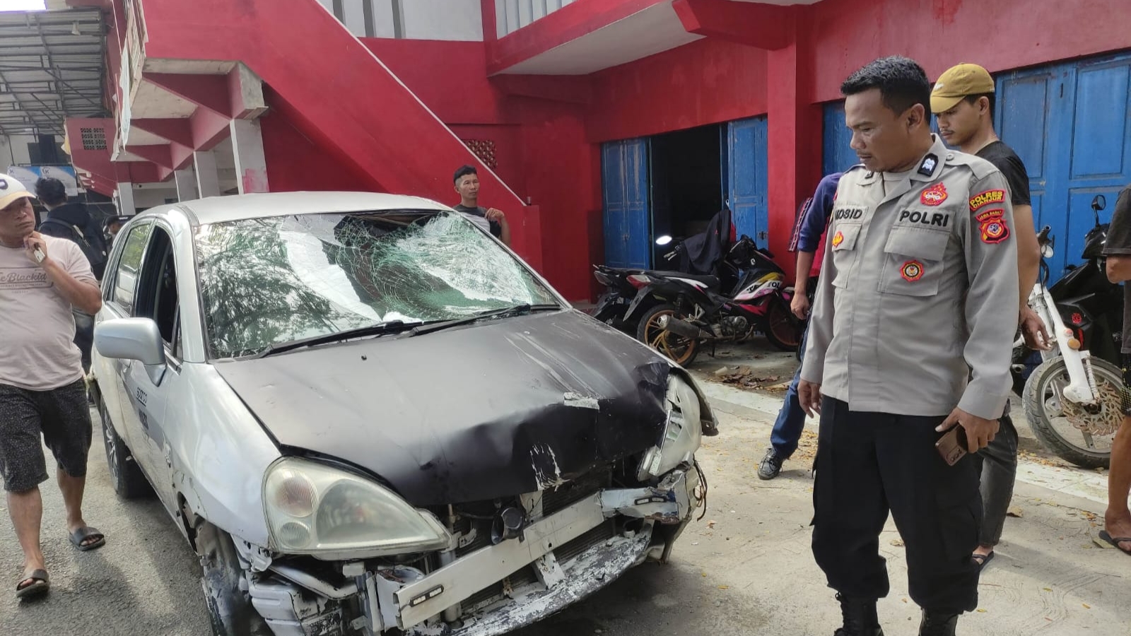 Teks: Kondisi mobil rusak bagian depan akibat kecelakaan lalu lintas saat diperiksa petugas kepolisian di lokasi kejadian.