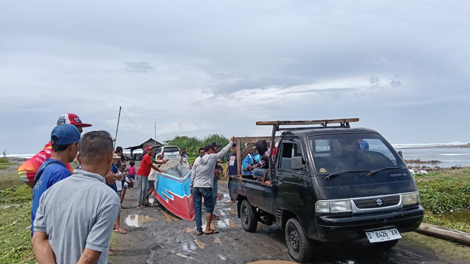 Teks: Warga dan petugas mengevakuasi perahu nelayan yang terdampar di Pantai Suliwa Cidaun menggunakan kendaraan bak terbuka.