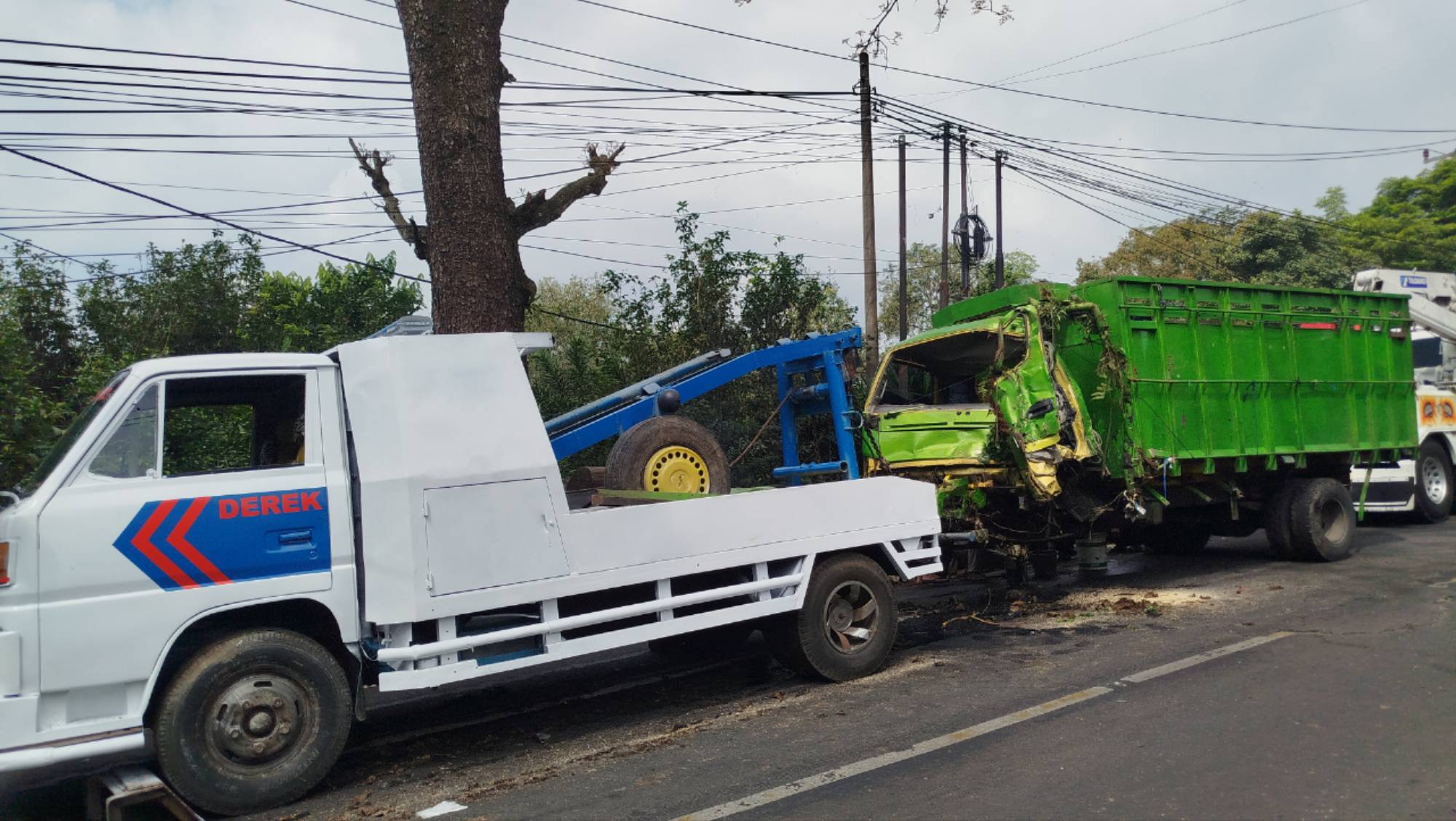 Teks: Truk rusak parah dievakuasi menggunakan derek di lokasi kecelakaan Cugenang