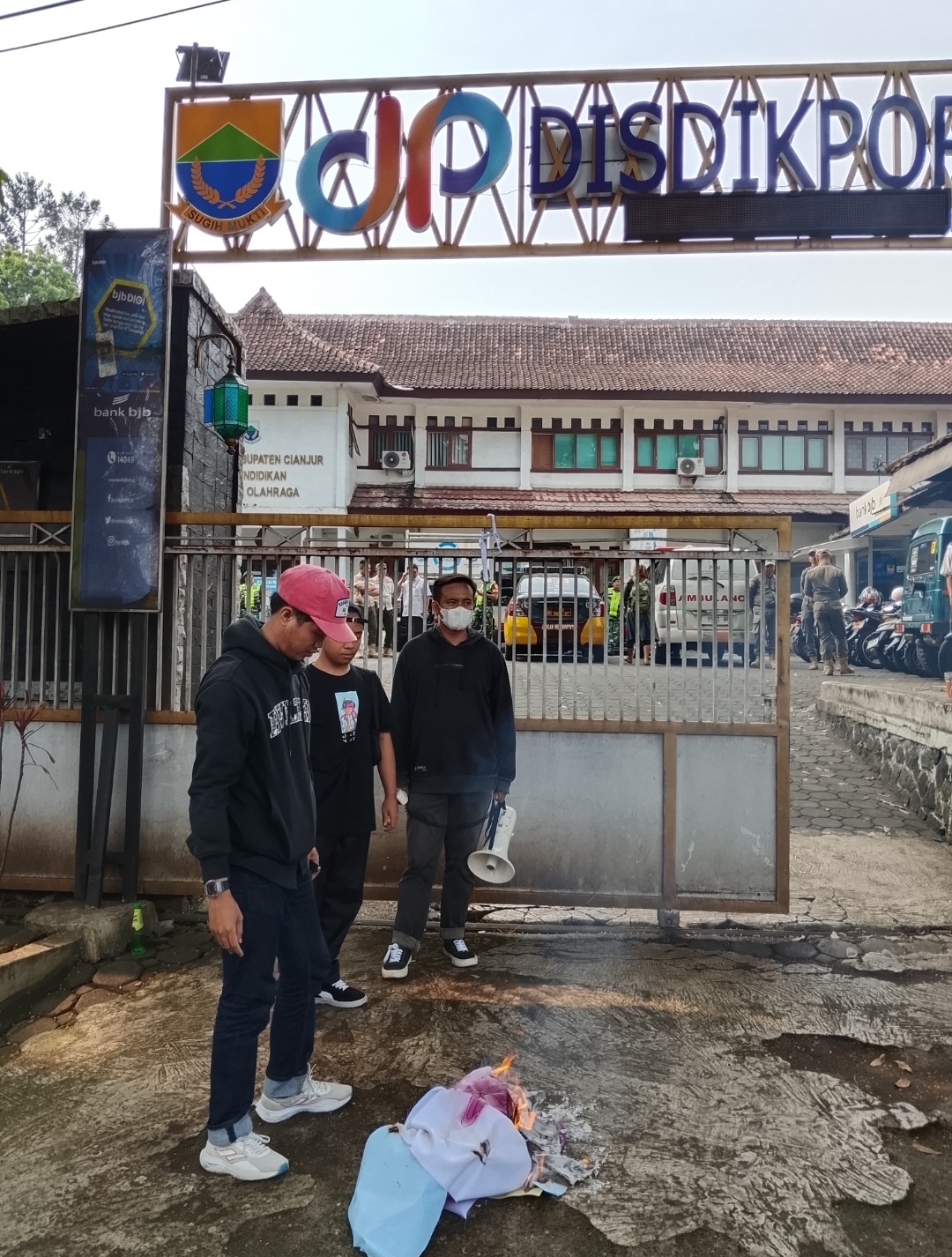 Teks: Aksi unjuk rasa LKMMC di depan Disdikpora Cianjur dengan pembakaran berkas sebagai simbol protes dugaan pungli pendidikan