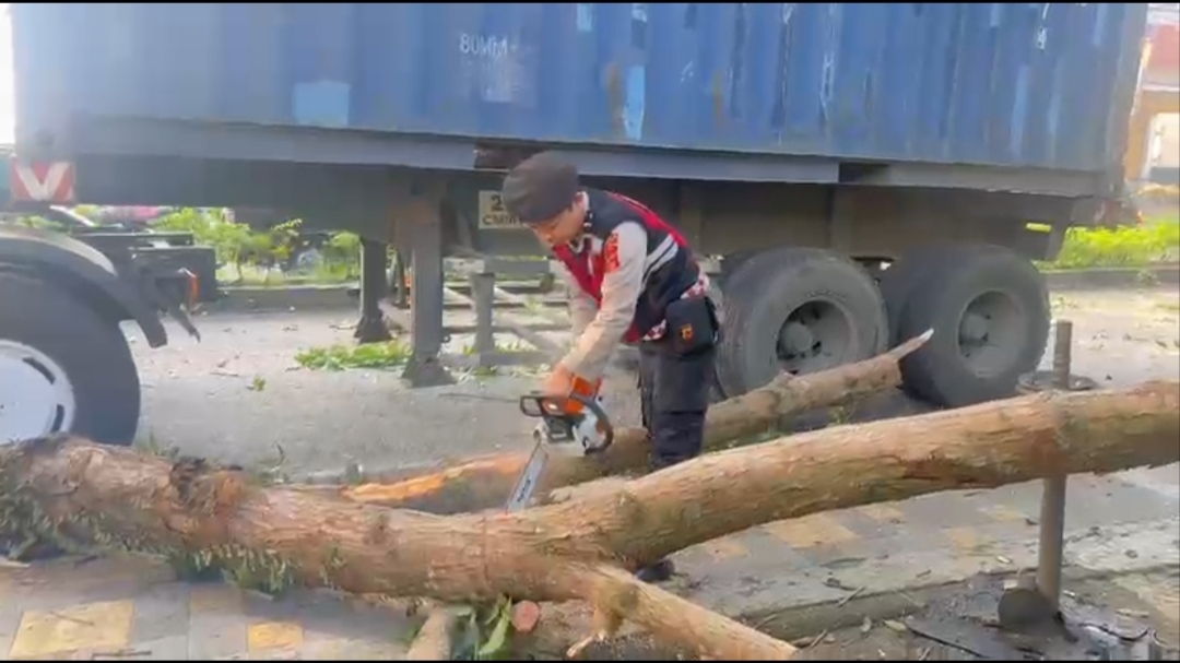 Teks: Polisi mengevakuasi truk kontainer yang tersangkut pohon di Jalan Abdullah Bin Nuh Cianjur.