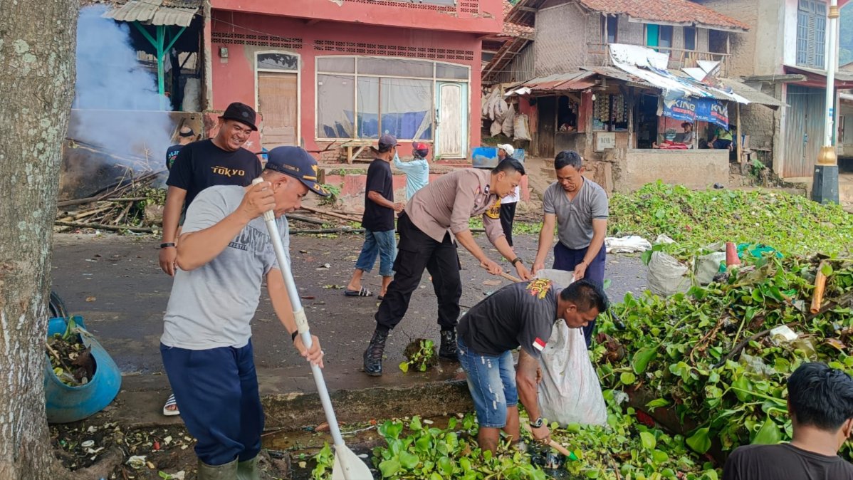 Teks: Personel Polsek Mande dan warga membersihkan eceng gondok di Waduk Jangari Cianjur.